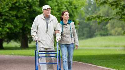 Senior man with walker walking in a park with a caregiver