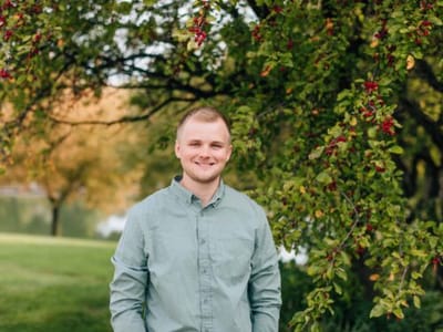Person smiling outdoors under a tree