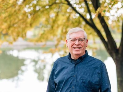 A smiling man standing outdoors near a lake