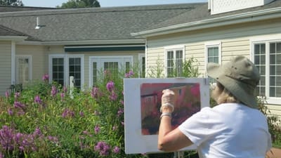 A resident painting outside surrounded by flowers