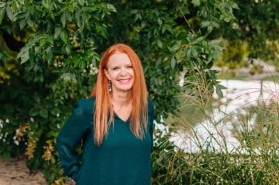 Smiling woman in a green shirt standing by greenery