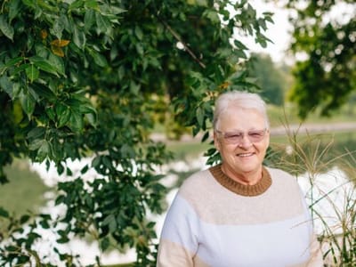Senior woman smiling near a lake surrounded by greenery