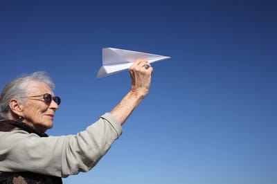 An older woman launching a paper airplane outdoors