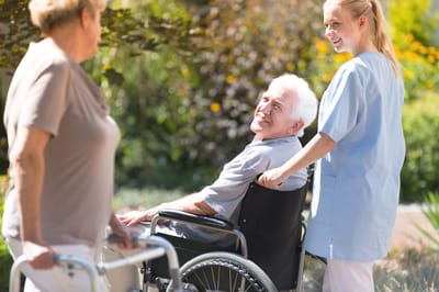 Staff assisting a smiling resident in a garden