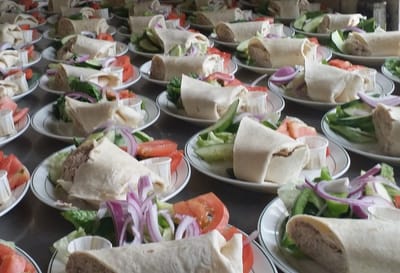Plates of wrapped sandwiches and salad on a table