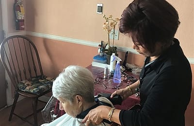 A caregiver giving a haircut to a resident in an interior space