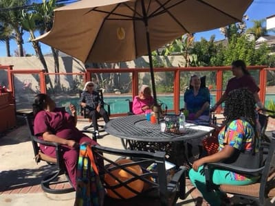 Residents and staff enjoying time outdoors under an umbrella