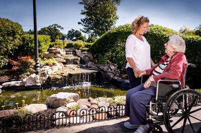 A caregiver with a resident by a garden with a waterfall