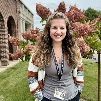 Staff member smiling outdoors in front of flowering shrubs