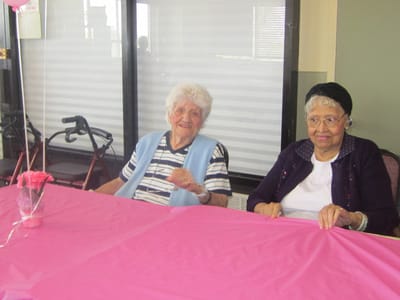 Two residents smiling at a table with pink decor