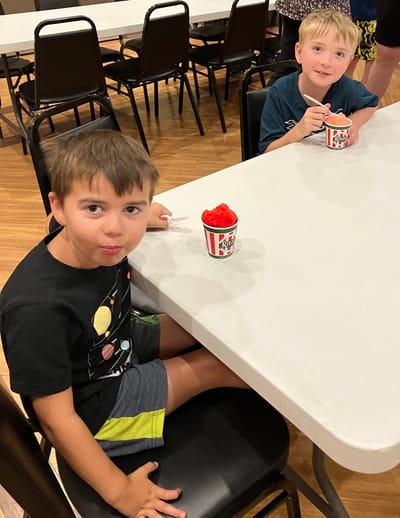 Two children enjoying snow cones at a table.