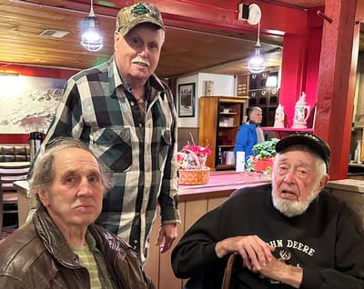 Three elderly men chatting indoors.