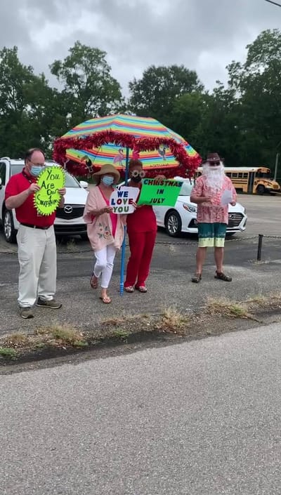 Staff and residents celebrate with signs under an umbrella.
