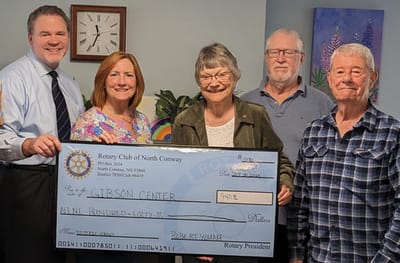 Group of people presenting a check donation in an indoor setting.