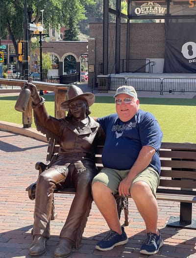 A man sitting next to a statue on a bench.