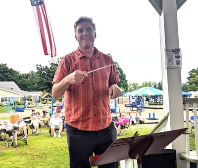 Conductor leading outdoor community event in park.