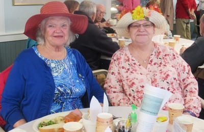 Two women enjoying a meal and wearing hats.