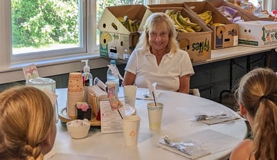 A woman smiling at a table with residents during a meal.