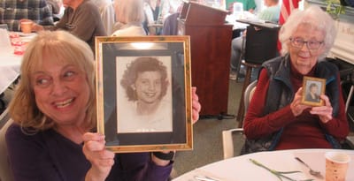 Two women holding framed photographs, smiling.