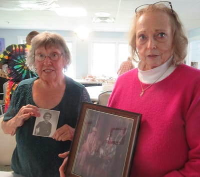 Two women holding old photographs in a communal area.