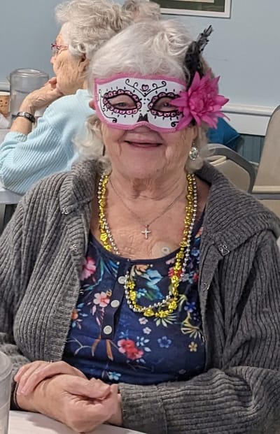 Elderly woman celebrating with mask and necklace.