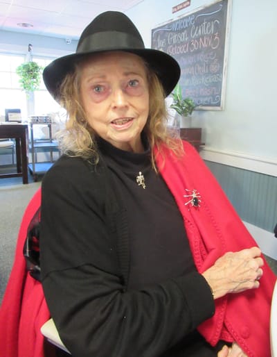 Resident with a black hat and red shawl in common area.