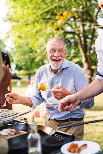A senior man smiling while grilling outdoors.