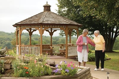 Two elderly women enjoy time in a garden gazebo.
