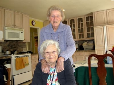 Two elderly women sharing a moment in the kitchen.