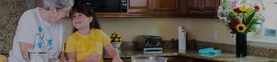 An elderly woman and a young girl enjoying time together in a kitchen.