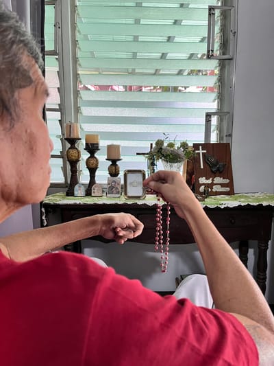 A resident holding rosary beads in a sunlit interior