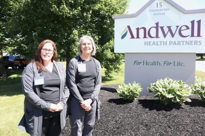 Two staff members standing by the facility sign.