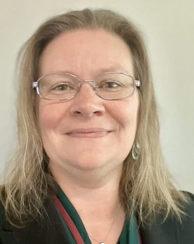 A woman smiling with glasses and blonde hair.