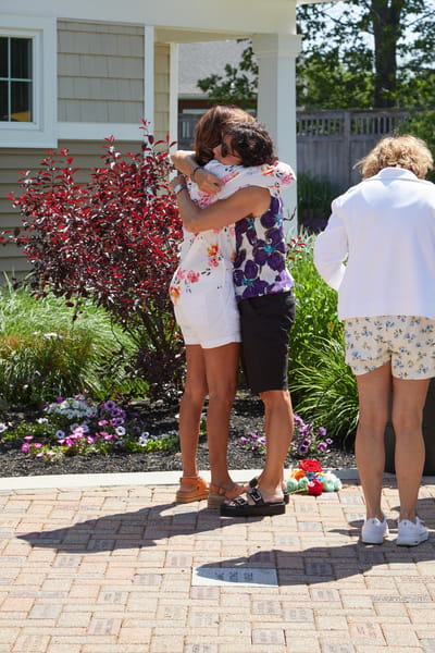 Two residents embrace outdoors in a garden setting.