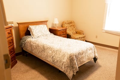 A simple bedroom with a bed and chair