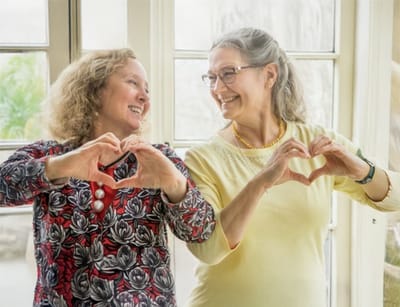 Two residents making heart shapes with their hands in a bright room