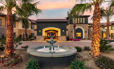Exterior view of a senior living facility with palm trees and fountain.