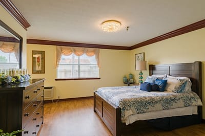 A well-furnished private resident room with a bed and dresser