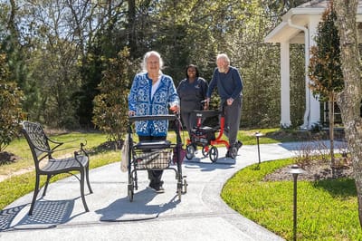 Residents walking outside with walkers on a landscaped pathway