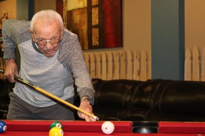 An elderly man playing billiards in a common area