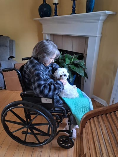 Resident in a wheelchair holding a small dog indoors