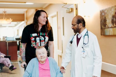 A doctor interacting with a resident and staff member in a hallway