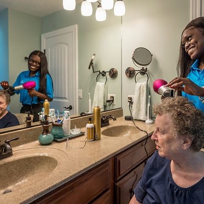 A caregiver styling a resident's hair in a bathroom