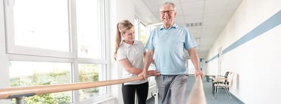 Riverside Manor, nursing home in Ames, IA — Senior resident walking with therapist along a hallway
