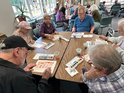 Residents engaged in a watercolor painting activity at a communal table.