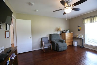 A private room with a chair and dresser in a senior facility