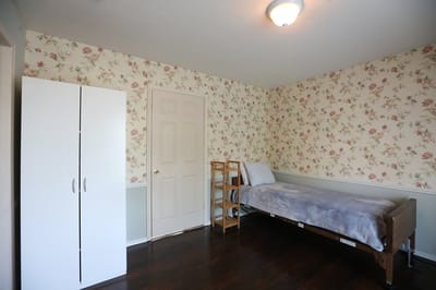 A simple resident room with floral wallpaper and a bed