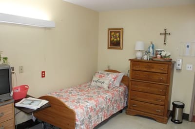 Simple interior of a resident's private room with bed and furniture