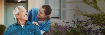 Caregiver assisting a resident outdoors with flowers