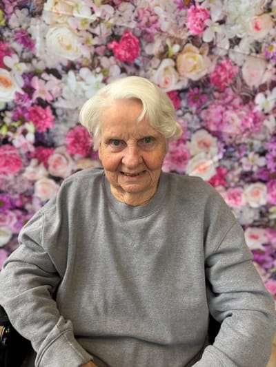 Senior resident smiling in front of floral backdrop